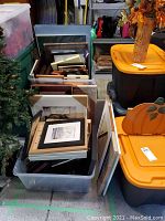 Three large plastic tubs filled with assorted picture frames in wood, metal, and glass at varying sizes.