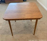 Full view of the square wooden folding table with tapered legs, showing overall shape and condition.