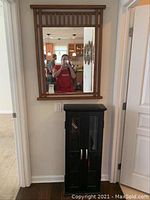 Full view of cabinet below mirror with black finish and beveled glass doors with silver handles.