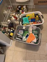 Four bins and containers filled with assorted cleaning supplies, cloths, and chemicals on floor by shelving unit.