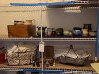Photo of shelf with pottery mini vases, cups, and small vases, with lace doilies in wire baskets below