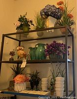 Shelf display of all faux florals, planters, Fenton bear, and other items included in the lot