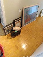 View of all items including framed prints leaning against the wall, the carved mask placed inside the metal mesh waste basket