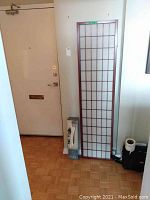Tall privacy screen with wooden frame and grid patterned translucent panel leaning against wall near door.