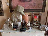 Full dresser top showing all items in lot, assortment of hats, figurines, mirror, cups, dishes, vase.