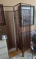 Full view of the bamboo three-panel room divider standing upright indoors, showing its height and panel structure.