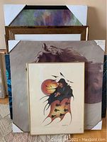 Five pieces of framed and unframed wall art stacked showing different styles and sizes.