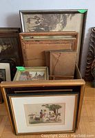Pile of framed prints and cardboard box stacked on floor