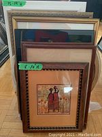 Photo of stacked framed prints showing one front print with two ethnic-style figures in red and brown dress surrounded by floral elements