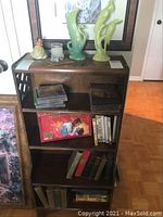 Full view of wooden shelf with multiple items including green ceramic bird figurines, candle, CDs, DVDs, and books
