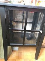 Front view of small black wooden cabinet with glass paneled door featuring grid design.