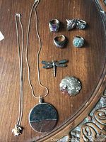 Full lot view showing two necklaces, two brooches, and five rings arranged on a wood surface.