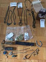 Photo showing assorted hematite necklaces, bracelets, brooches, earrings, and amethyst geode on parquet floor.