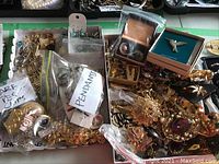 Overview of costume jewelry assortment with labels indicating pendants and scarf ties clips, showing variety of metal-tone pieces and boxes with brooches.
