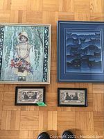Five framed pieces arranged on floor showing cross stitch embroidery, large bamboo print, cat print, and two small embroidered works.