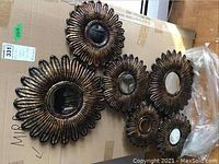 Six-piece metal wall art set shown on cardboard box, sunflower petal design with round bevelled mirrors inside each piece