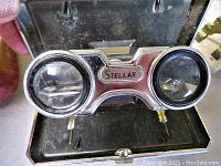 Close-up of Stellar branded folding binoculars with coated lenses in a black case