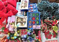 Wide shot showing multiple boxes of assorted vintage glass Christmas ornaments, string lights, ribbons, bows, and other decorations piled together on a festive poinsettia fabric background.