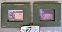 Two framed folk art paintings side by side, featuring a cow and a pig in rustic green wooden frames.