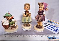 Three Goebel Hummel figurines; Which hand?, For Mother, Playmates, arranged in a row with size ruler showing scale.