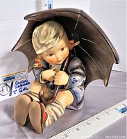 Front and side view of the Goebel MJ Hummel Umbrella Girl figurine showing the detailed painting and size compared to a measuring tape.