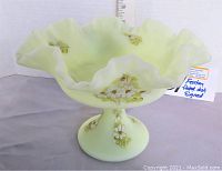 Side view of the yellow satin Fenton pedestal dish showing floral decoration and ruffled edge with a ruler in background for height measurement.