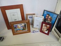 Six assorted photo frames in different sizes and styles arranged on a shelf, some with decorative prints inside.