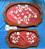 Full view of two vintage signed wood trays with paper flower needlework artwork on red fabric under glass. Both trays have leather handles and decorative brass accents.