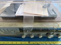 Front view of the Emerson stereo turntable featuring 8 track, AM/FM radio tuner, control knobs, and a plastic dust cover taped closed with manuals inside.