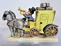Frontal view showing two gray horses harnessed to a yellow mail carriage with a lad in blue jacket blowing a horn.