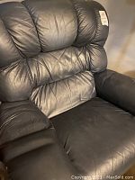Close-up view of the padded backrest and armrest of the dark gray leather recliner chair.