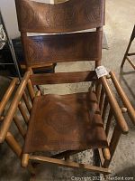 Full view of the hand tooled leather sling chair with rounded wood construction, showing seat and backrest panels and armrests.