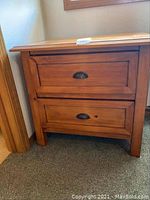 Front view of wooden nightstand showing two drawers with metal half-moon handles and natural wood finish.