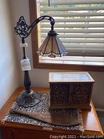 Photo of vintage stained glass lamp, decorative jewelry box, and wooden paddle on a patterned cloth surface under window blinds.