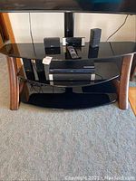 Photo of black TV stand with three glass shelves, Sony Blu-ray player on middle shelf with remote, Bose speakers arranged on shelves.
