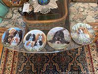 Four Royal Box Cavalier King Charles Spaniel decorative plates laid out showing dog illustrations, each with gold trim edges.
