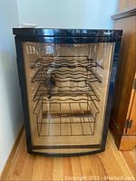 Front view of the black Haier wine fridge showing the curved glass door and internal metal racks for storing wine bottles.