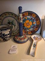 Overview of lot showing all items together: two decorative Mexican ceramic plates, a tall pottery candle holder, a floral-patterned pitcher, and a spoon rest with bird design.