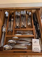 View of ornate flatware set neatly organized in a wooden drawer tray with a visible lot tag