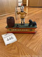 Front view of trick dog mechanical bank showing clown, dog, barrel on green base with front label 'TRICK DOG'
