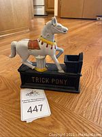 Front and side view showing white pony on black base with coin slot and coin pan, 'TRICK PONY' lettering on side.