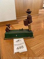 Side view showing man figurine holding briefcase and monkey on green metal base with 'MONKEY BANK' embossed.