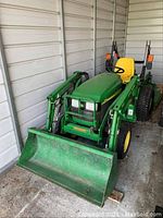 Front three-quarter view of green John Deere tractor with loader bucket attached.