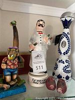 Photo showing the musical bottle shaped like a man with mustache holding two wine bottles, colorful dinosaur figurine, and blue and white ceramic bottle.