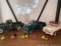 Three Dodge model trucks in green, dark green, and white/red colors lined up on a shelf with five small toy vehicles in front