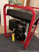 Oblique view of generator showing red tubular steel frame, black fuel tank, Briggs & Stratton engine