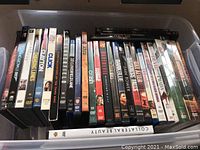 Top view of a plastic bin filled with DVD movies, standing upright side by side so titles visible.