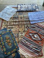 Photo showing five assorted rugs laid out on floor: large floral 5x8 carpet, kilim rug, and three smaller floral bath rugs.