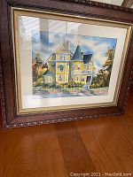 Framed watercolor painting showing yellow Victorian house with turret, matted and in ornate dark wood frame.