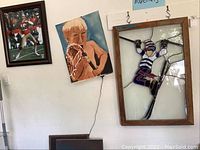 Photo showing three framed wall art items displayed on a wall: stained glass of skier, watercolor lacrosse player, and football sports photo.